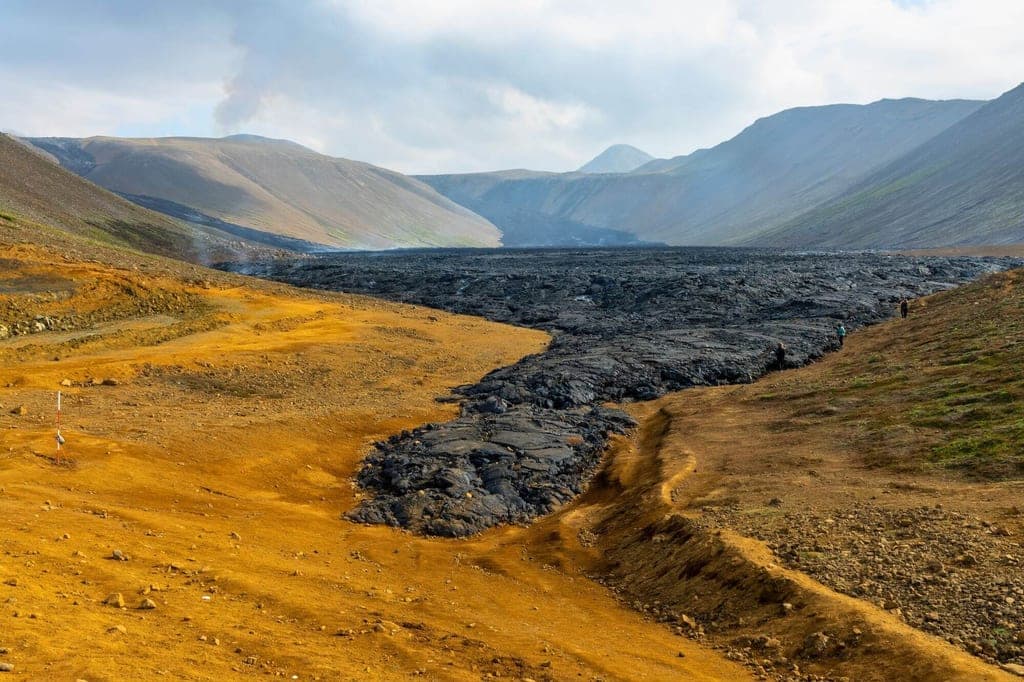 Weite Vulkanlandschaft mit erkaltetem Lavafluss und goldbraunem Plateau unter bewölktem Tageslicht