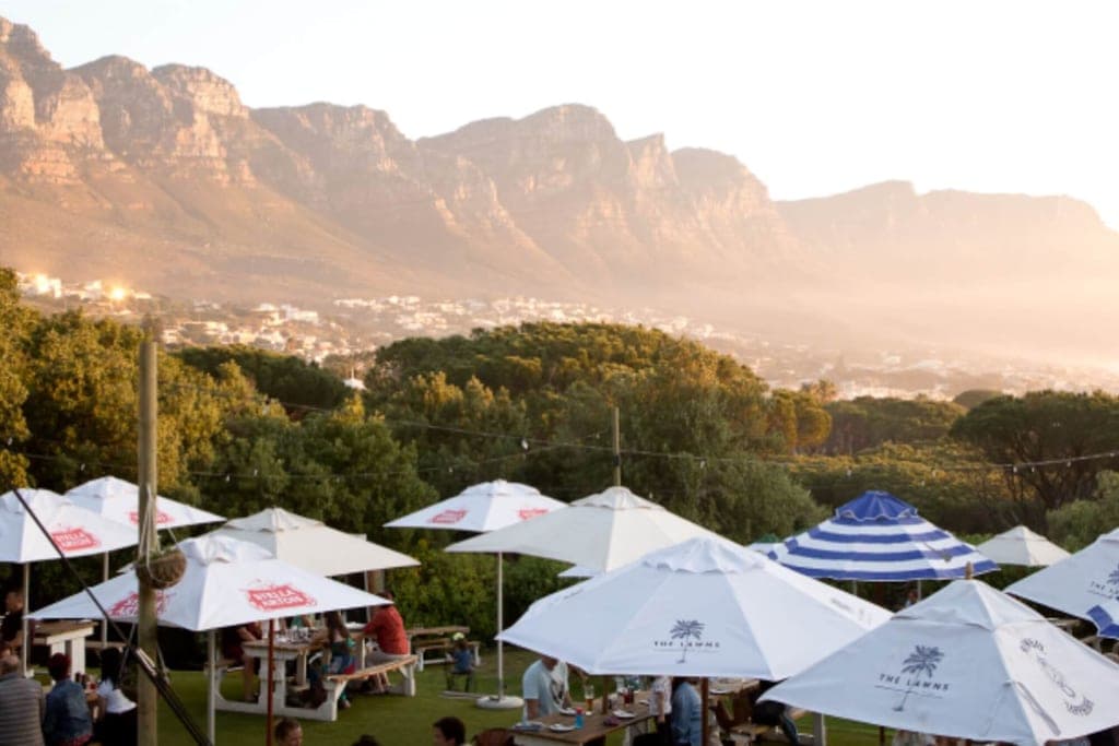 Outdoor-Restaurant mit Sonnenschirmen vor einer Bergkette im warmen Abendlicht