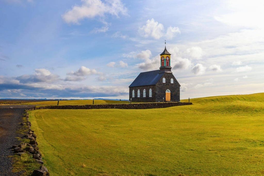 Schwarze Holzkirche mit buntem Turm auf weitem grasbewachsenen Gelände unter hellem Himmel.