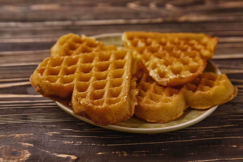 Nahaufnahme mehrerer herzförmiger Waffeln auf einem Teller auf dunklem Holztisch.
