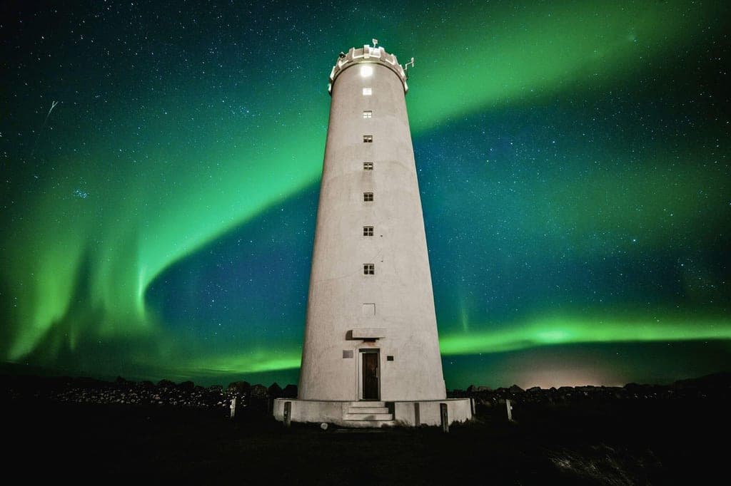 Weißer Leuchtturm vor grünem Nordlicht und sternklarem Nachthimmel