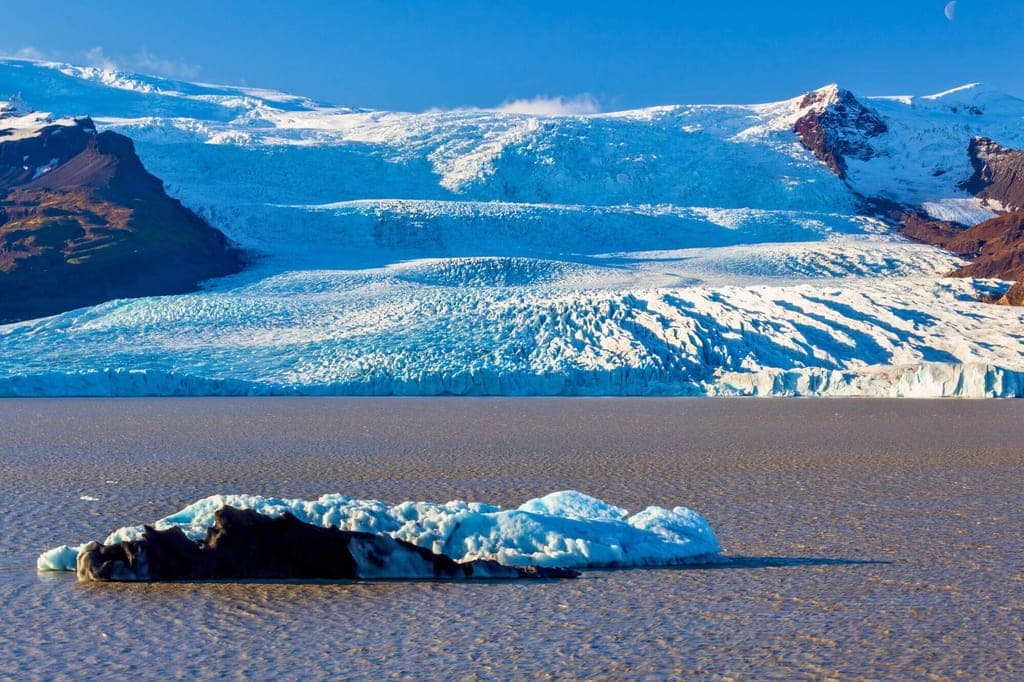 Kleiner Eisbrocken auf ruhigem Wasser vor einer breiten Gletscherfront im klaren Seitenlicht