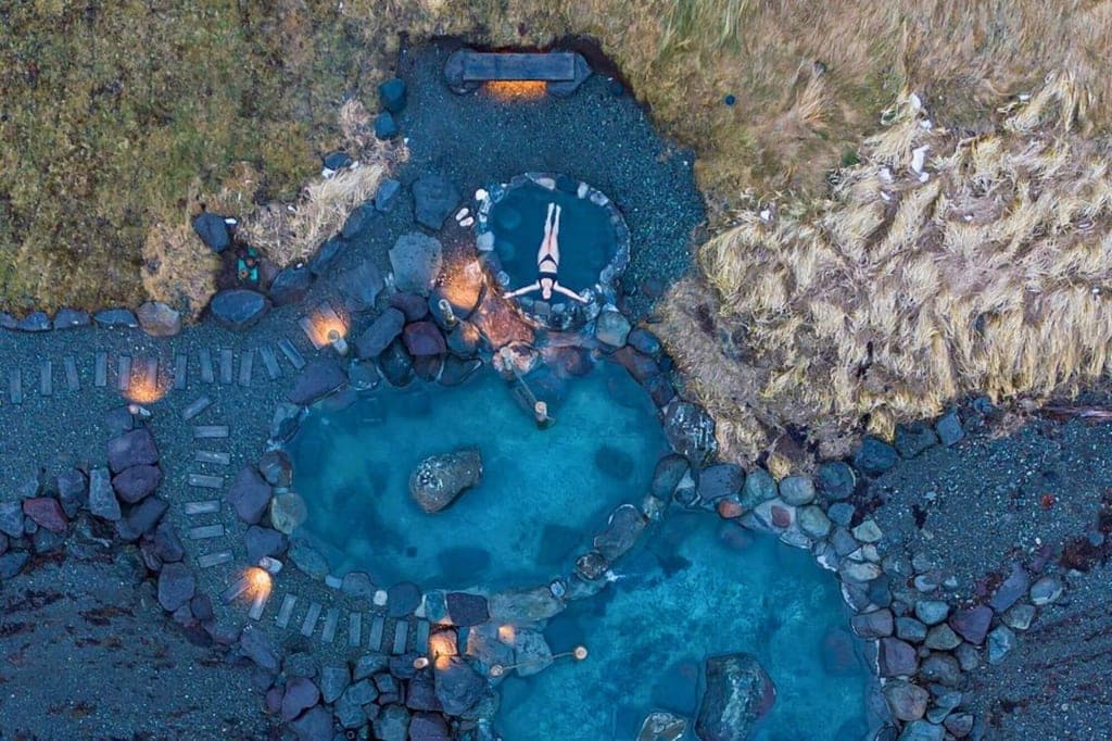 Drohnenbild von mehreren heißen Quellen mit einer Person, die in einem kleinen Rundbecken liegt.