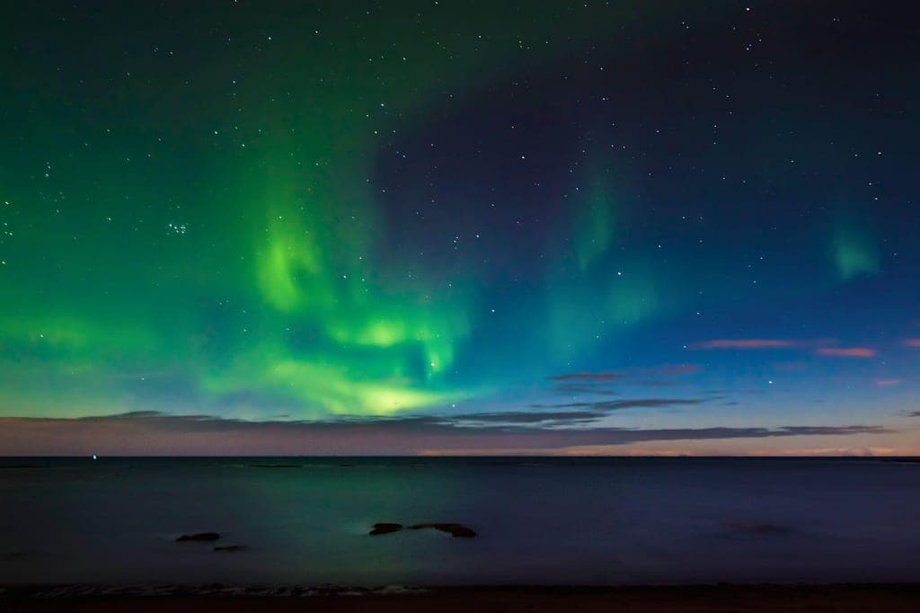 Grün leuchtendes Polarlicht über ruhiger Nachtsee am Küstenhorizont.