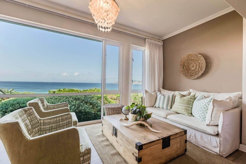 Helles Wohnzimmer mit Sofa, Sesseln und großem Fenster mit Blick auf das Meer.