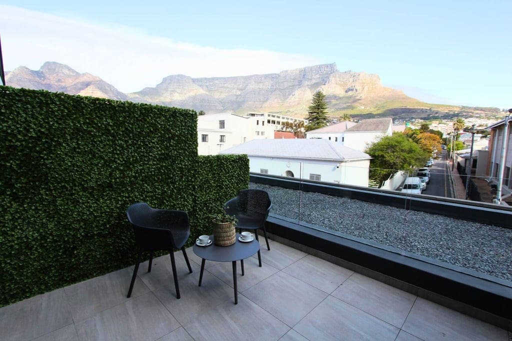 Dachterrasse mit zwei Stühlen, kleinem Tisch und Blick auf Häuser und markanten Bergkamm im Hintergrund.