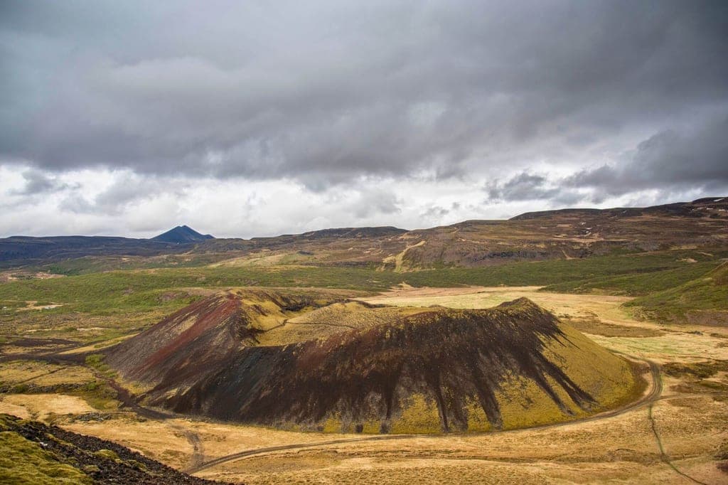 Halbkreisförmiger Vulkankrater in braun-gelber Landschaft unter schwerem, bewölktem Himmel