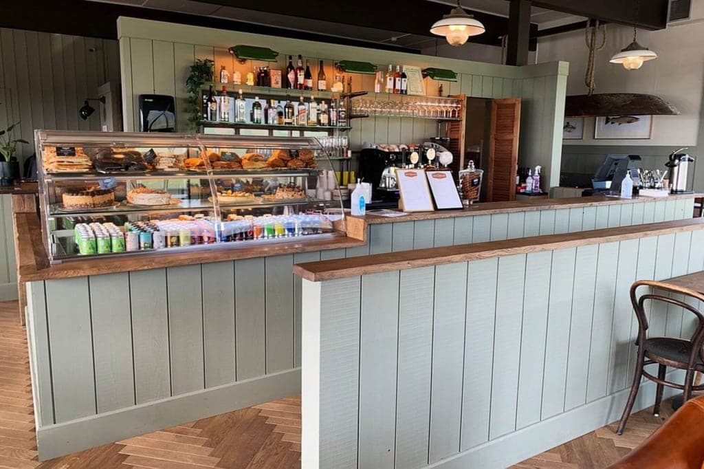 Innenansicht eines Cafés mit Kuchenvitrine und hellgrünem Holztheken-Tresen.