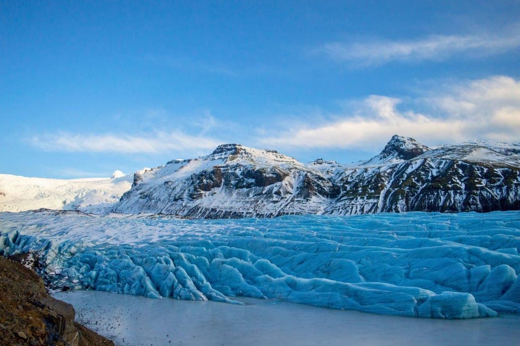 Blauer Gletscher im Vordergrund vor schneebedeckten Bergen bei klarem Tageslicht.
