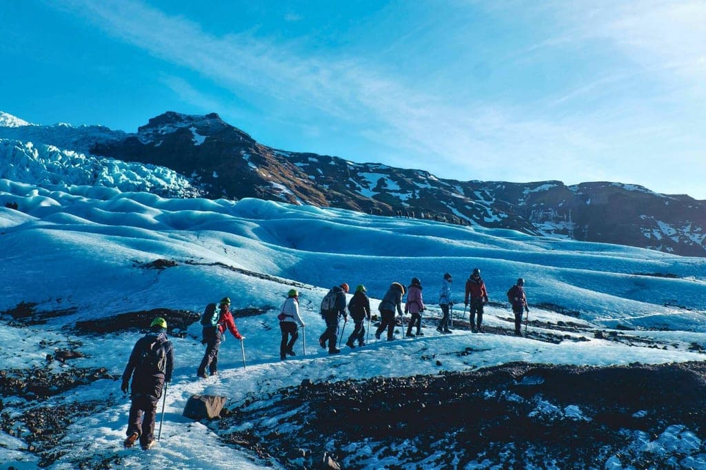 Gruppe von Wanderern mit Ausrüstung bewegt sich über wellige Gletscherflächen bei klarem Himmel.