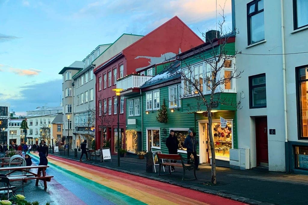 Straßenszene in Reykjavík mit bunten Häusern und einem regenbogenfarbenen Fußgängerweg bei Dämmerung.