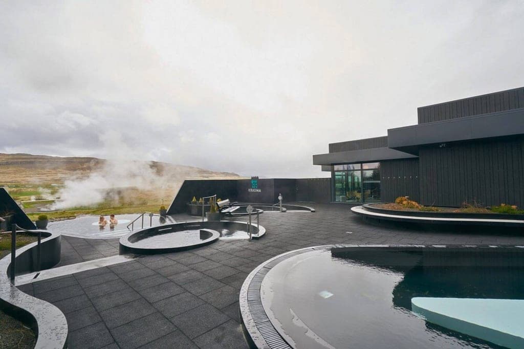 Außen-Thermalbecken und modernes schwarzes Spa-Gebäude bei bewölktem Himmel