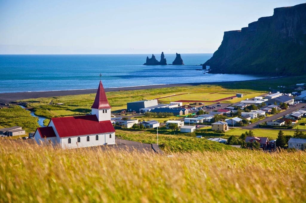 Küstendorf mit weißer Kirche und rotem Dach vor Meer, Felsnadeln und Klippen im Hintergrund