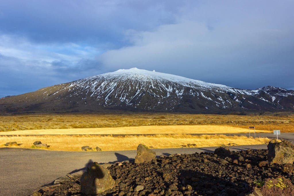 Schneebedeckter Berg auf der Snæfellsnes-Halbinsel, vulkanische Felsen und warmes Abendlicht