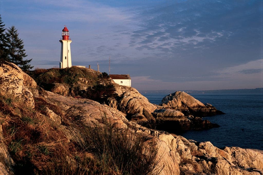 Leuchtturm auf einer felsigen Küste im warmen Abendlicht, ruhiges Meer und weiter Himmel